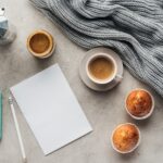 top view of cup of coffee with muffins, blank paper and smartphone with instagram app on screen on